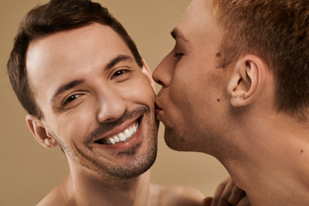 Two young men embrace joyfully while sharing a tender kiss, radiating happiness together.の写真素材