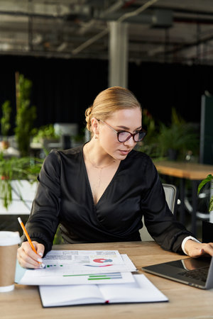 A dedicated young woman reviews documents on her laptop in a bright office.
