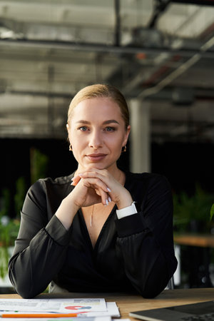 A young, confident plus size woman focuses on her work at her office desk, surrounded by greenery.