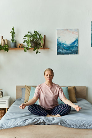 Relaxation fills the air as a young woman meditates peacefully on her bed in a serene space.の写真素材