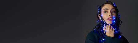 A young woman playfully draped in glowing blue lights poses confidently in a dim room.の写真素材