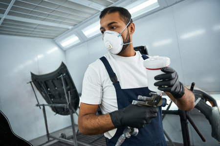 A young mechanic in work gear readies a spray gun for painting in the workshop.の写真素材