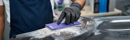 A skilled mechanic is sanding the surface of a car with focus and precision in a bustling garage.