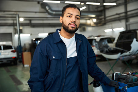 Handsome young mechanic stands confidently while working in a bright and busy garage area