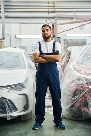 Handsome mechanic stands with arms crossed in a modern garage, showcasing his expertise and style.の写真素材