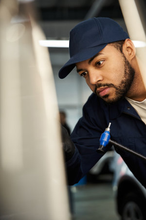 A dedicated young mechanic intently fixes a vehicle in a tool filled repair shop.の写真素材