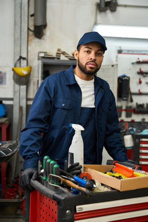 Handsome young mechanic focuses on his task in a busy garage, surrounded by tools and machinery.