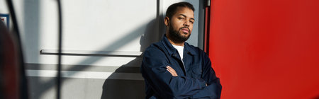 Handsome young mechanic leans against a wall, showcasing skill and determination in his work.の写真素材