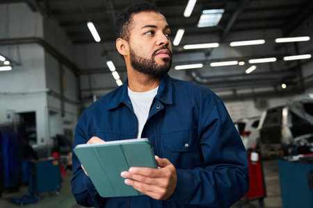 Handsome young mechanic reviews his work schedule in a modern automotive repair shop.の写真素材