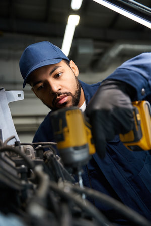 Handsome mechanic focuses intently on fixing machinery while using power tools in the garage.の写真素材