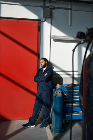 Young mechanic stands confidently with arms crossed, exuding charm in a bright workshop.の写真素材