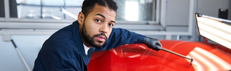 A skilled young mechanic repairs a car in a modern workshop with bright lighting.の写真素材