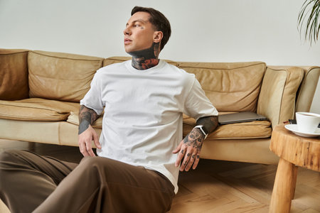 The handsome man relaxes indoors, showing off his tattoos in a peaceful moment.の写真素材