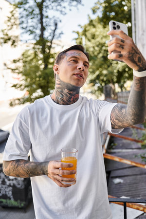 A young, handsome man at home captures a moment with his phone, savoring a refreshing drink.の写真素材