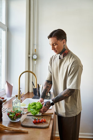 In a bright kitchen, a young man skillfully chops lettuce, embracing healthy cooking.の写真素材