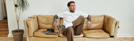 A young handsome man sits casually on a sofa, enjoying his time at home, relaxed and stylish.の写真素材