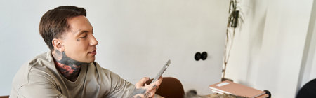 A young man with tattoos enjoys a leisurely moment, engaged in texting at home.の写真素材