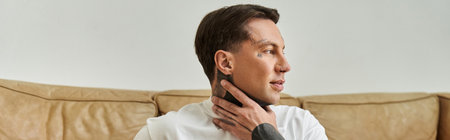 A young man sits peacefully at home, contemplating life while seated on a warm, inviting couch.の写真素材