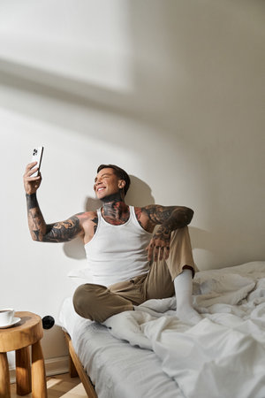 A young, handsome man enjoys a cheerful moment at home, sitting on his bed and taking a selfie.の写真素材