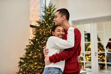 A couple smiles and embraces in their cozy, decorated apartment for the holidays.の写真素材