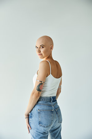 A young bald woman with alopecia stands confidently against a plain backdrop, embracing her beauty.
