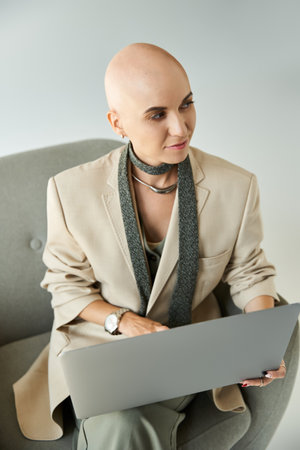 A confident young bald woman works on her laptop, showcasing her unique style and resilience.の写真素材