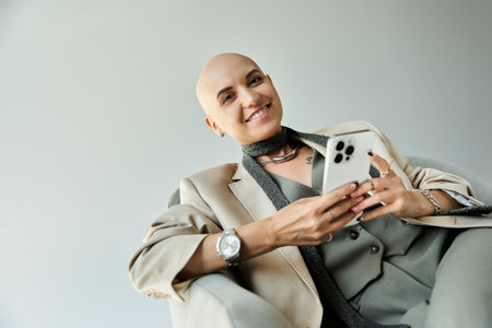 A young bald woman radiates confidence as she smiles while using her smartphone.の写真素材