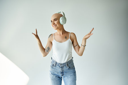A young bald woman smiles broadly while wearing headphones, expressing happiness in a bright space.