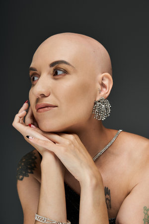 A confident young woman with a bald head admires her reflection, wearing elegant earrings.の写真素材
