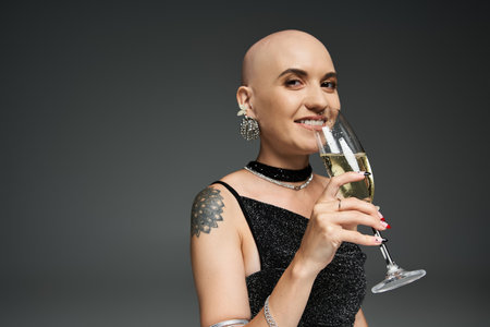 A young bald woman smiles warmly while holding a glass of champagne in a chic setting.の写真素材
