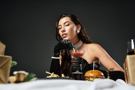 A stunning woman dressed elegantly savors gourmet food while sipping a stylish drink.の写真素材