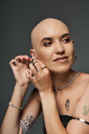 A confident young bald woman with alopecia skillfully puts on earrings while showcasing her style.の写真素材