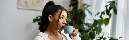 A beautiful young woman sips a warm drink as she focuses on her studies in her home.