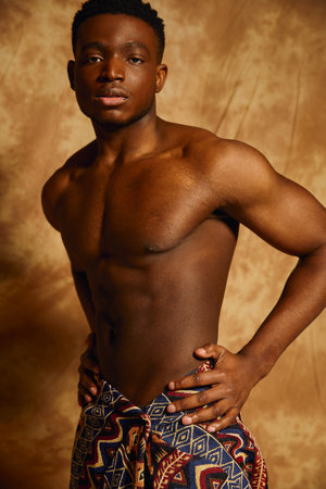 In a captivating artistic backdrop, a young handsome African American man poses confidently. With a bare chest and a stylish wrap, he exudes charisma and strength, embodying vibrant energy.の写真素材