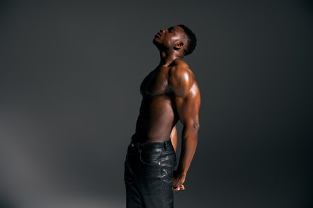 A young handsome African American man stands confidently with a powerful pose, showcasing his physique in a studio.の写真素材