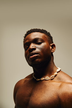 A young handsome African American man poses topless, showcasing a confident expression. His unique necklace adds a touch of charm to the artistic atmosphere, creating an engaging visual moment.の写真素材