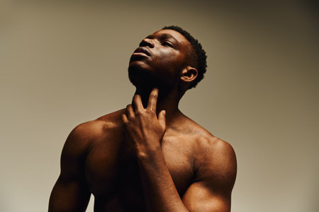 A young handsome African American man poses topless, expressing confidence and introspection. The soft lighting highlights his features, creating an artistic and captivating atmosphere.の写真素材
