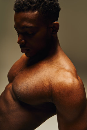 A young African American man stands with a confident posture, highlighting his toned physique. The warm lighting enhances his features, creating an artistic and captivating atmosphere.の写真素材