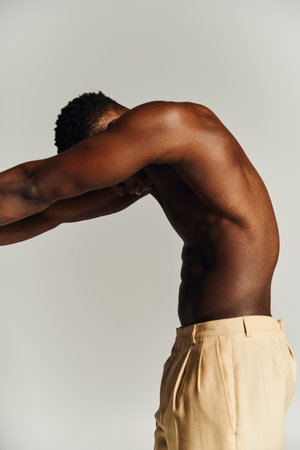 A young handsome African American man showcases his physique by posing topless in a simple studio environment, embodying strength and confidence during a creative photoshoot.の写真素材