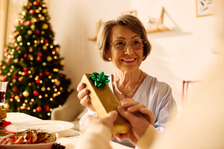 A happy senior couple enjoys a cozy Christmas celebration, exchanging gifts by the decorated tree.の写真素材