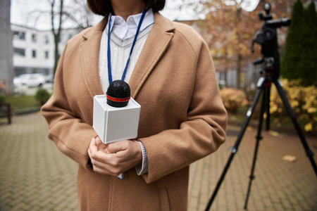 A focused journalist holding a microphone stands outdoor, preparing to deliver a news report amid autumn foliage.の写真素材