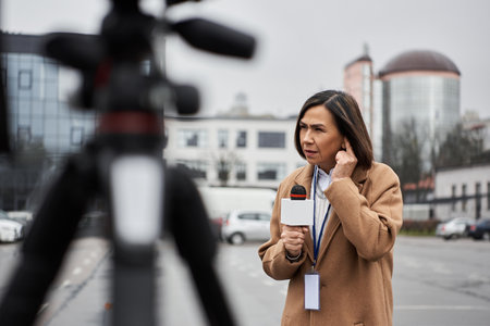 A focused female journalist holds a microphone, preparing to deliver breaking news amid an urban...