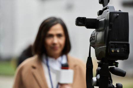 A multiracial female journalist wears a beige coat, confidently addressing the camera with a microphone in hand.の写真素材