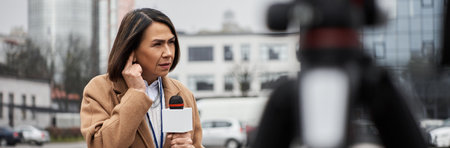A multiracial female journalist speaks into a microphone while preparing for a live news report outdoors.の写真素材
