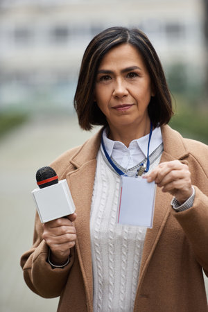 A multiracial female journalist confidently holds a microphone and displaying her press badge