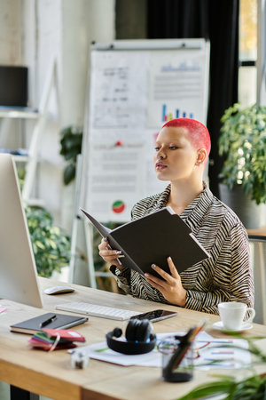 A bald woman with vibrant pink hair studies papers at her desk, surrounded by plants.の写真素材