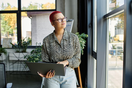 A bald woman with vibrant hair enjoys a moment of reflection while working in a stylish office.