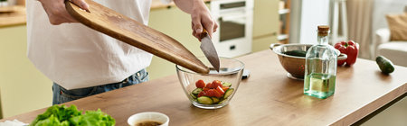 A young man mixes fresh ingredients in a bowl, embracing a healthy kitchen lifestyle.の写真素材