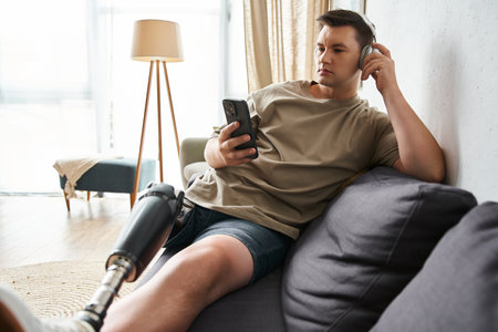Young man on a couch, headphones on, focused on his smartphone and enjoying music.