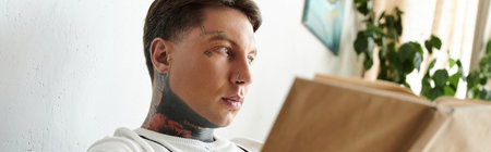 Man with tattoos deeply engaged in his book while sitting comfortably indoors.の写真素材